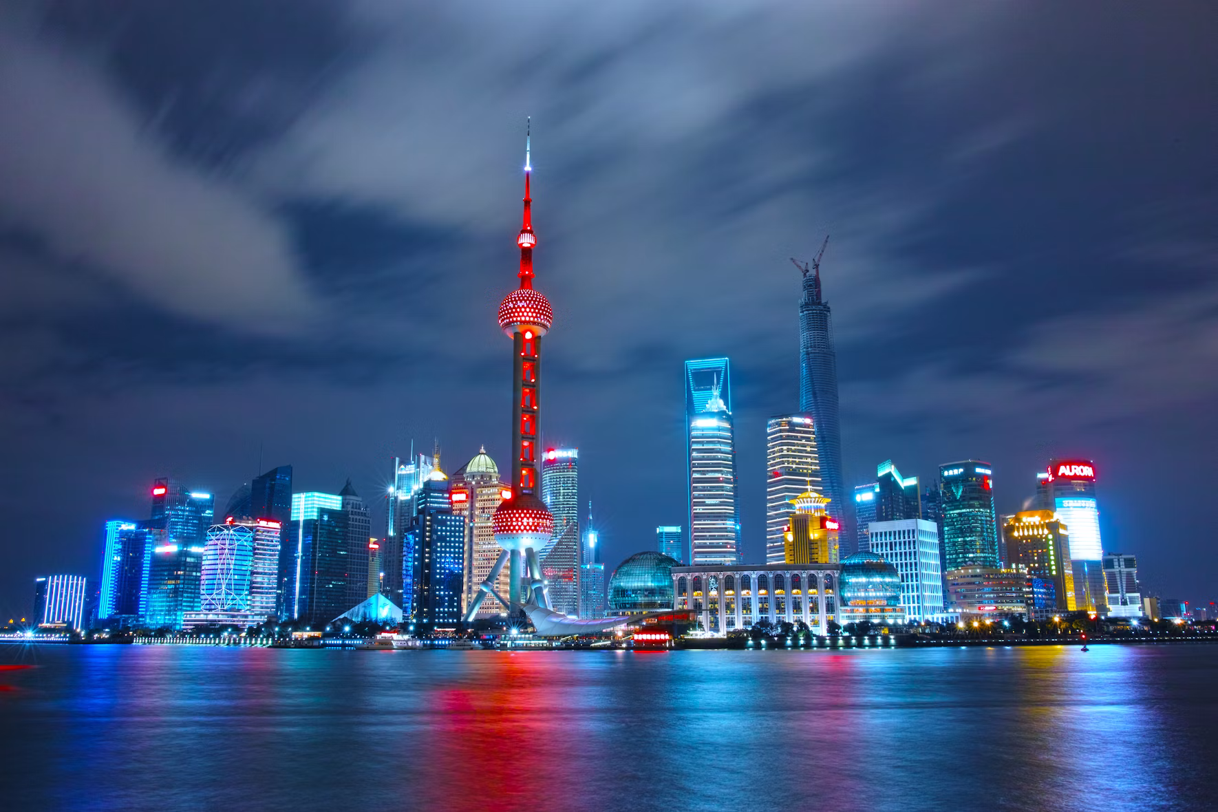 The illuminated Shanghai Pudong skyline at night, with the Oriental Pearl Tower reflected in the Huangpu River