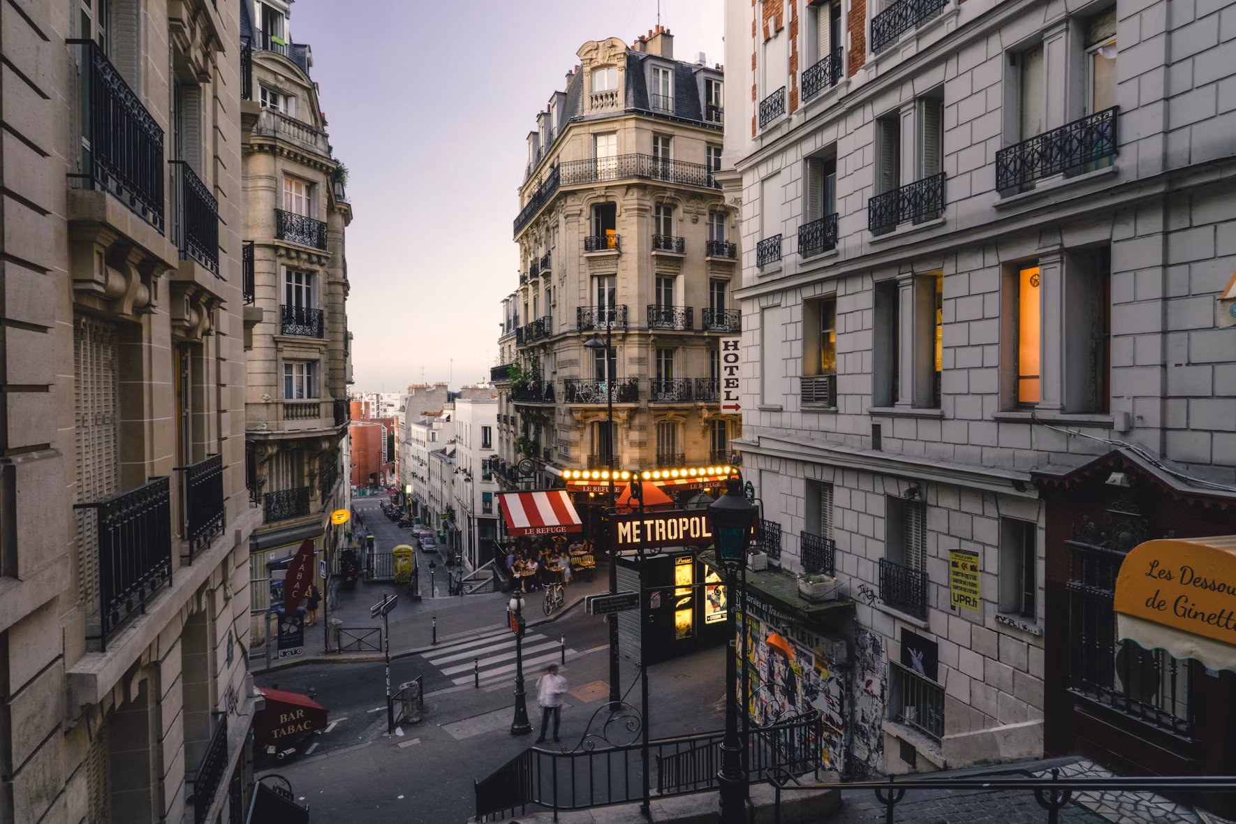 A Haussmann-era street corner in Paris at golden hour with a Métro entrance and cafés, France