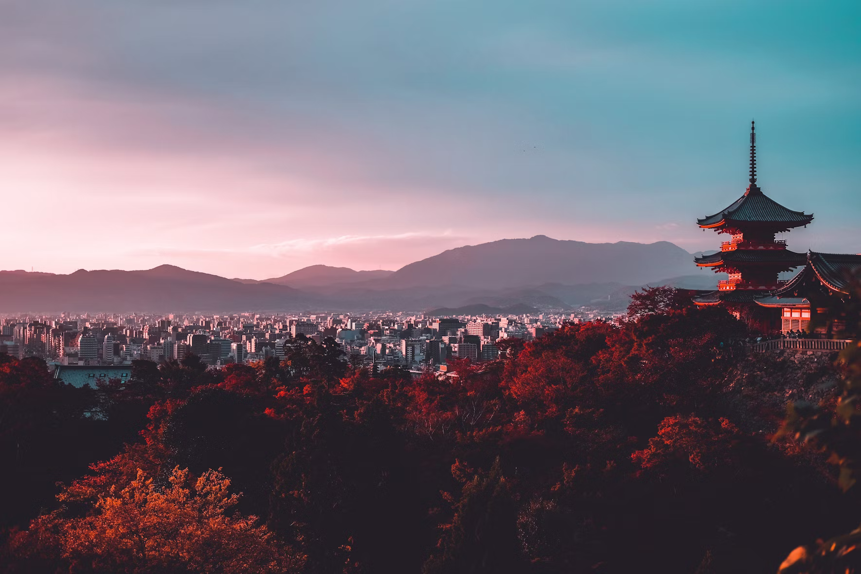 A three-storied pagoda above Kyoto at sunset with autumn foliage and the city and mountains beyond, Japan