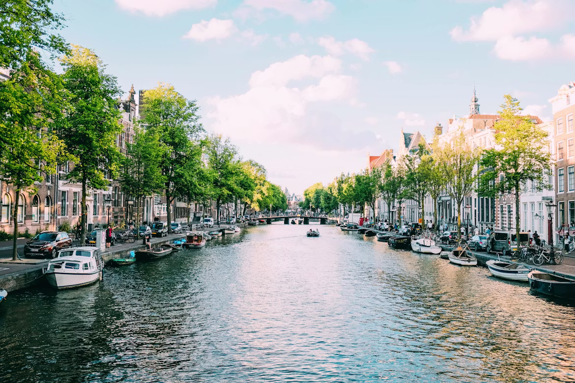 A tree-lined Amsterdam canal with boats and canal houses on a sunny day, Netherlands