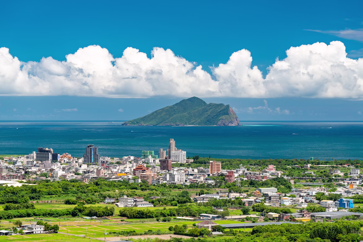 A coastal Taiwanese town with Turtle Island offshore under a blue sky, Taiwan